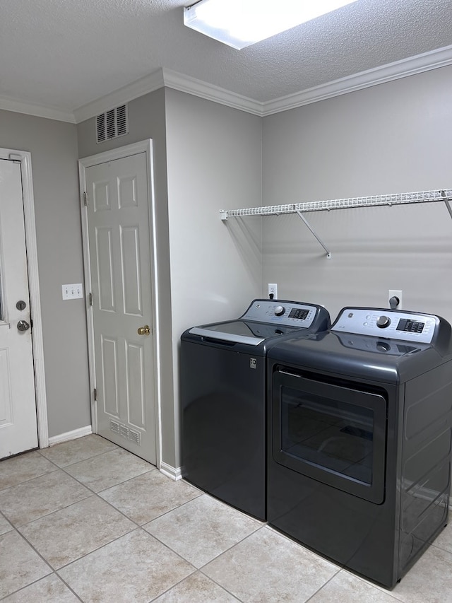 washroom featuring a textured ceiling, washing machine and dryer, light tile patterned floors, and crown molding