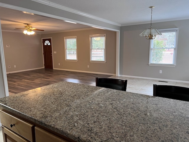 kitchen featuring tile patterned floors, a textured ceiling, ceiling fan with notable chandelier, crown molding, and decorative light fixtures