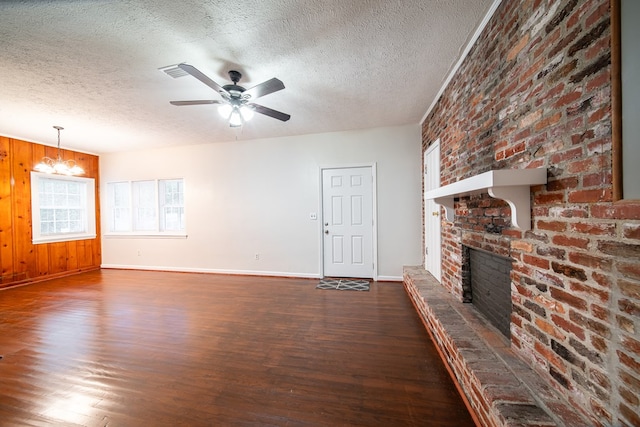 unfurnished living room featuring dark hardwood / wood-style floors, a textured ceiling, wooden walls, a fireplace, and ceiling fan with notable chandelier