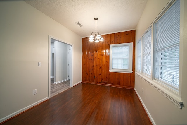 interior space with wood walls, dark hardwood / wood-style flooring, a textured ceiling, and a notable chandelier