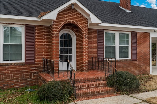 entrance to property featuring a shingled roof, brick siding, and a chimney