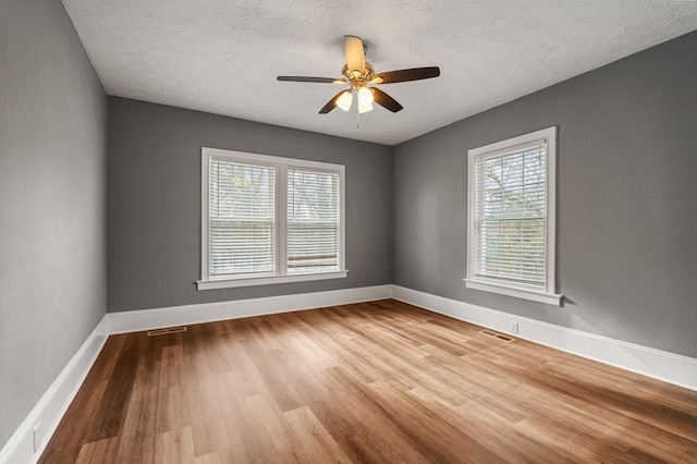 empty room with a healthy amount of sunlight, visible vents, baseboards, and wood finished floors