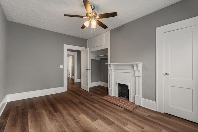 unfurnished living room featuring dark wood finished floors, a fireplace with raised hearth, ceiling fan, a textured ceiling, and baseboards