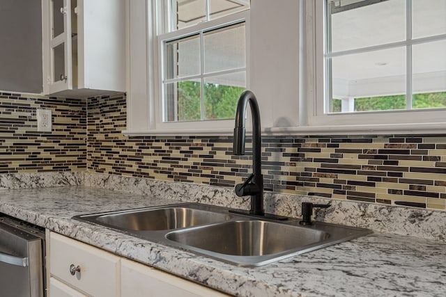 kitchen with light stone counters, a sink, white cabinets, decorative backsplash, and dishwasher