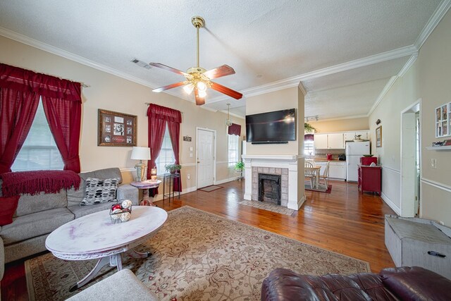 living room with a textured ceiling, a tiled fireplace, a ceiling fan, wood finished floors, and ornamental molding