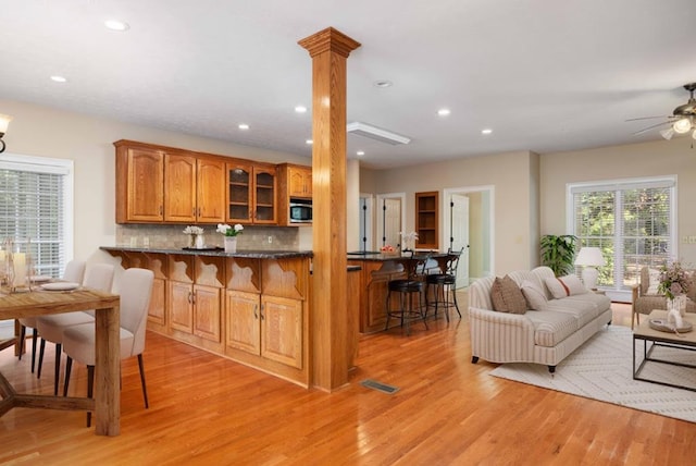 kitchen featuring backsplash, a kitchen breakfast bar, light hardwood / wood-style flooring, kitchen peninsula, and decorative columns