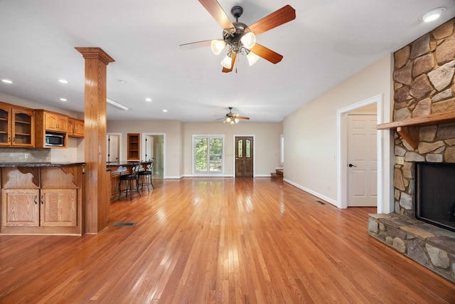 unfurnished living room with decorative columns, ceiling fan, a fireplace, and light hardwood / wood-style floors