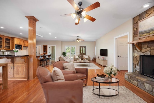 living room featuring ornate columns, ceiling fan, a fireplace, and light wood-type flooring