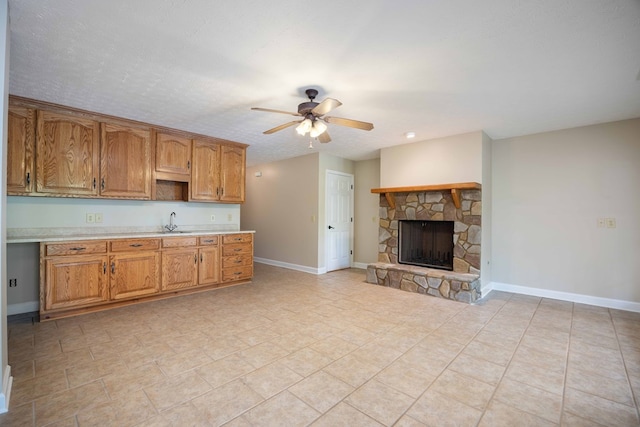 kitchen featuring a textured ceiling, ceiling fan, sink, light tile patterned floors, and a fireplace