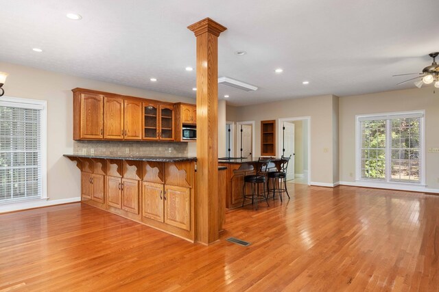 kitchen with a kitchen bar, kitchen peninsula, decorative columns, light hardwood / wood-style floors, and stainless steel microwave