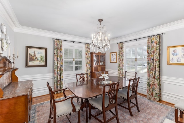 dining room with ornamental molding, wainscoting, wood finished floors, and a notable chandelier