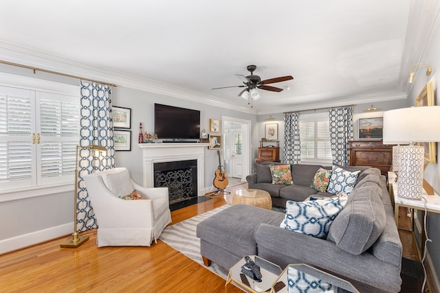 living room with baseboards, ceiling fan, crown molding, light wood-style floors, and a fireplace