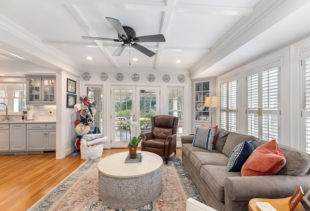 living area with coffered ceiling, a ceiling fan, french doors, beam ceiling, and light wood finished floors