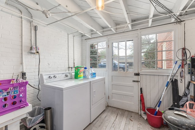 clothes washing area with laundry area, washing machine and dryer, brick wall, and light wood finished floors