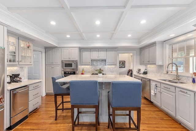 kitchen with a breakfast bar area, light wood-style flooring, coffered ceiling, a sink, and appliances with stainless steel finishes