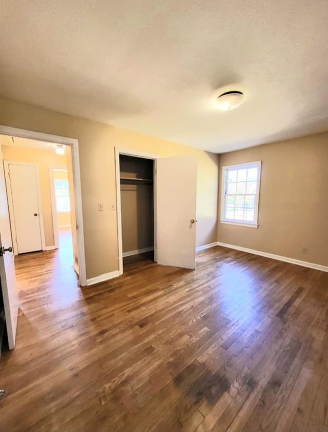 unfurnished bedroom featuring baseboards, a closet, dark wood-style flooring, and a textured ceiling