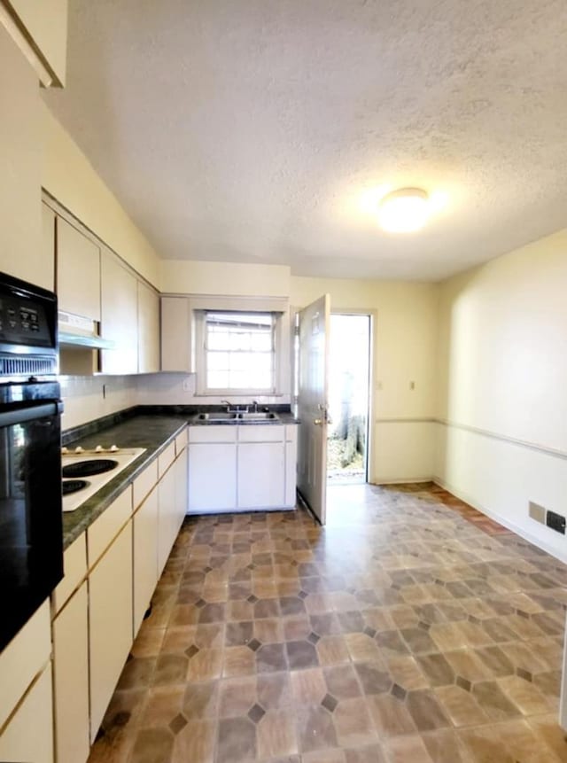 kitchen with dark countertops, under cabinet range hood, visible vents, oven, and white cooktop