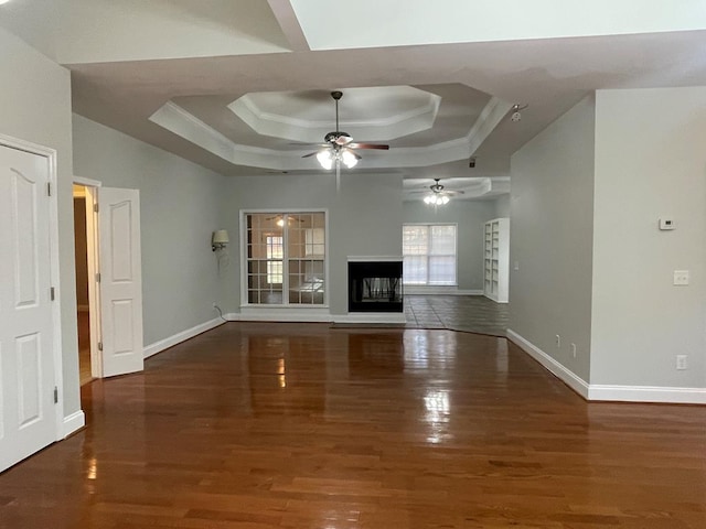 unfurnished living room with a multi sided fireplace, a raised ceiling, baseboards, and wood finished floors