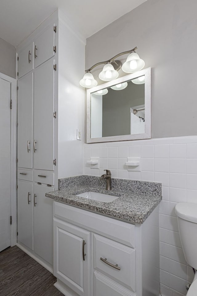 bathroom featuring a wainscoted wall, tile walls, toilet, vanity, and wood finished floors