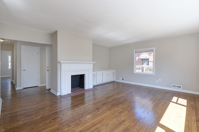 unfurnished living room with a fireplace with flush hearth, visible vents, and dark wood finished floors