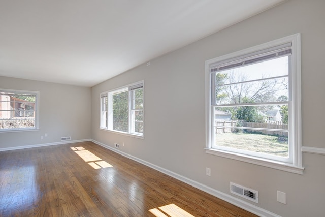 empty room with dark wood finished floors, visible vents, and baseboards