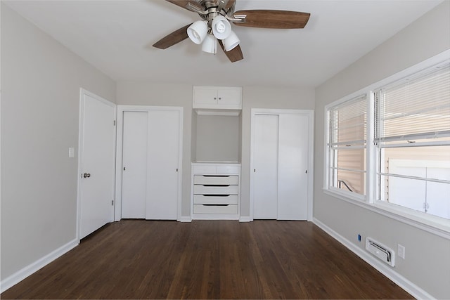 unfurnished bedroom with dark wood-style floors, two closets, visible vents, ceiling fan, and baseboards