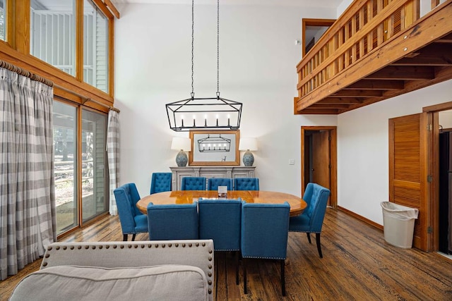 dining space with wood finished floors, a towering ceiling, baseboards, and a notable chandelier