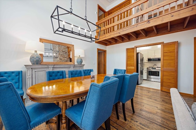 dining space with wood finished floors, a towering ceiling, and an inviting chandelier