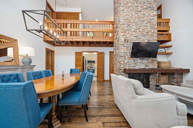 dining room with a towering ceiling, a fireplace, a chandelier, and dark wood finished floors