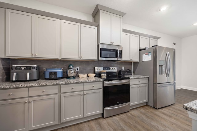 kitchen featuring tasteful backsplash, light stone counters, stainless steel appliances, and light hardwood / wood-style floors