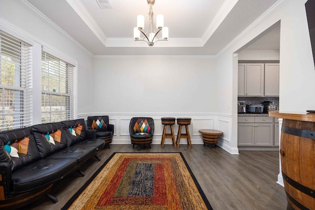 living room featuring dark wood-type flooring, ornamental molding, a tray ceiling, and a notable chandelier