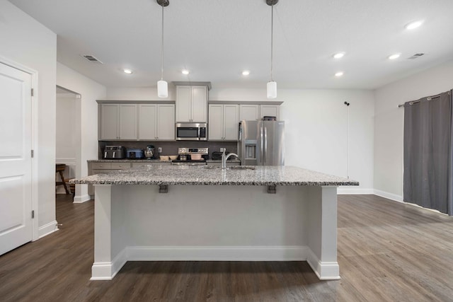 kitchen featuring pendant lighting, appliances with stainless steel finishes, gray cabinets, light stone counters, and a center island with sink