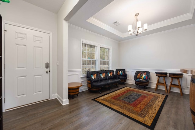 living room with crown molding, dark hardwood / wood-style flooring, a tray ceiling, and a chandelier