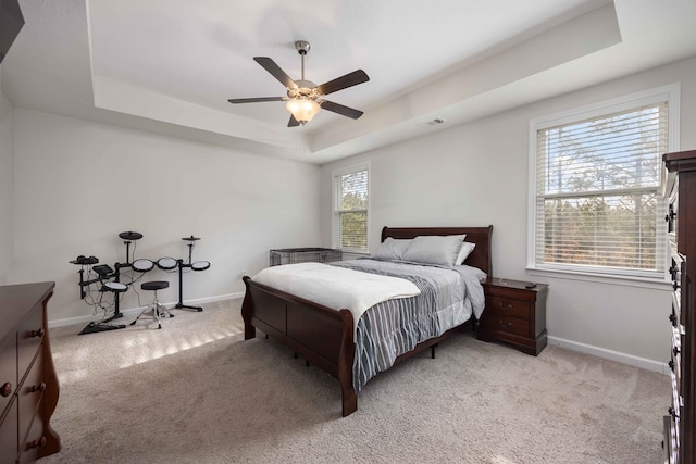 carpeted bedroom with ceiling fan and a raised ceiling