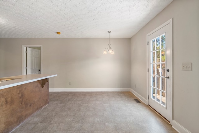 unfurnished dining area featuring a textured ceiling and a chandelier