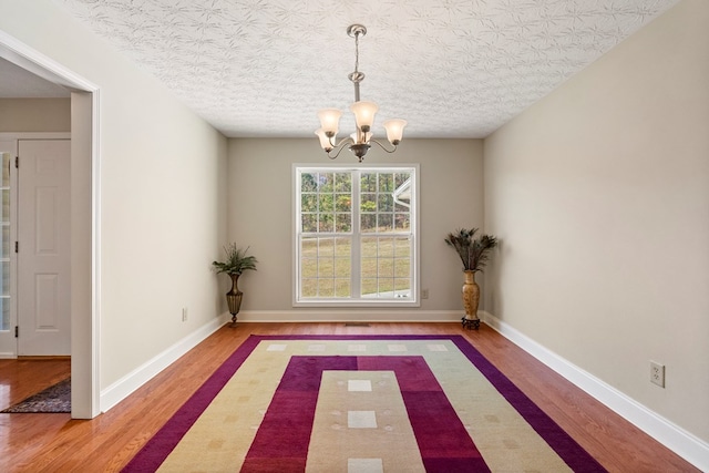 unfurnished dining area with a chandelier, a textured ceiling, and hardwood / wood-style flooring