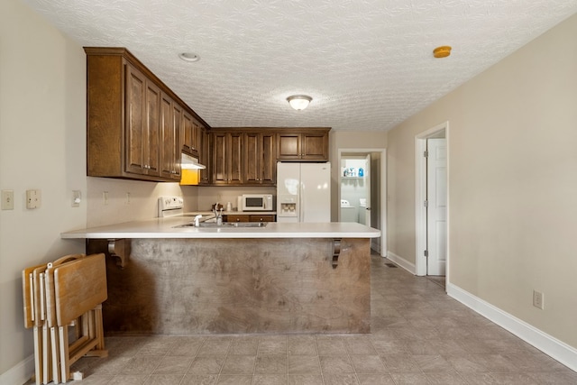 kitchen with a textured ceiling, kitchen peninsula, sink, and white appliances