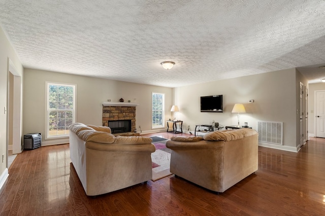 living room with hardwood / wood-style flooring, a stone fireplace, and a textured ceiling