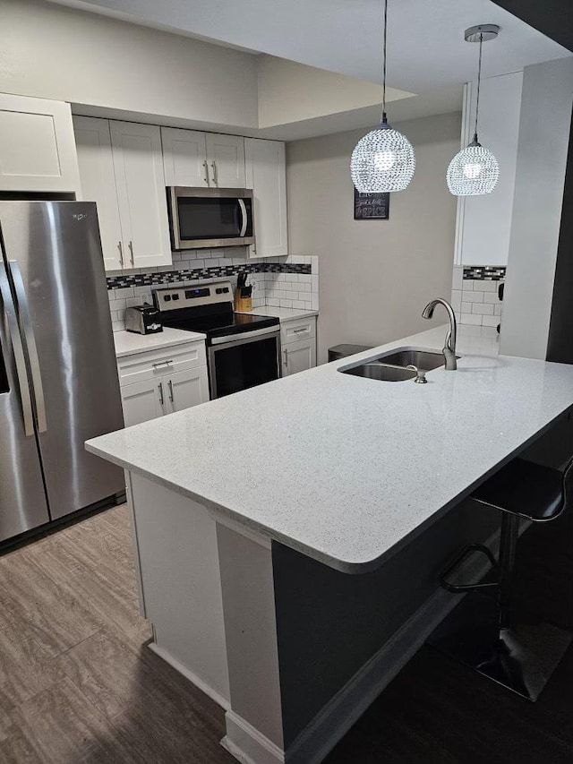 kitchen featuring kitchen peninsula, appliances with stainless steel finishes, sink, white cabinets, and hanging light fixtures