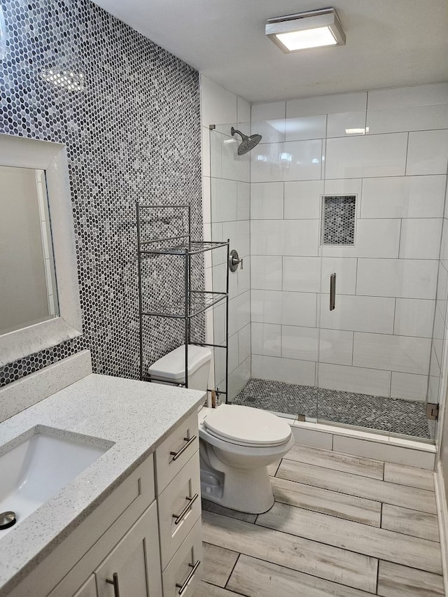 bathroom featuring vanity, toilet, a shower with door, and tile walls