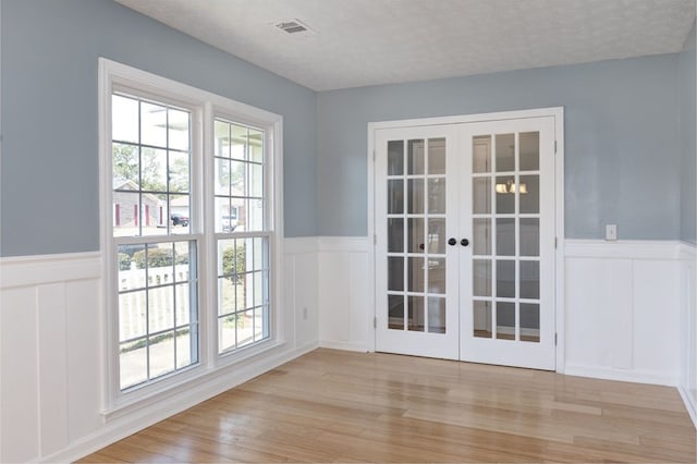 doorway to outside with wood finished floors, french doors, a wainscoted wall, and a healthy amount of sunlight