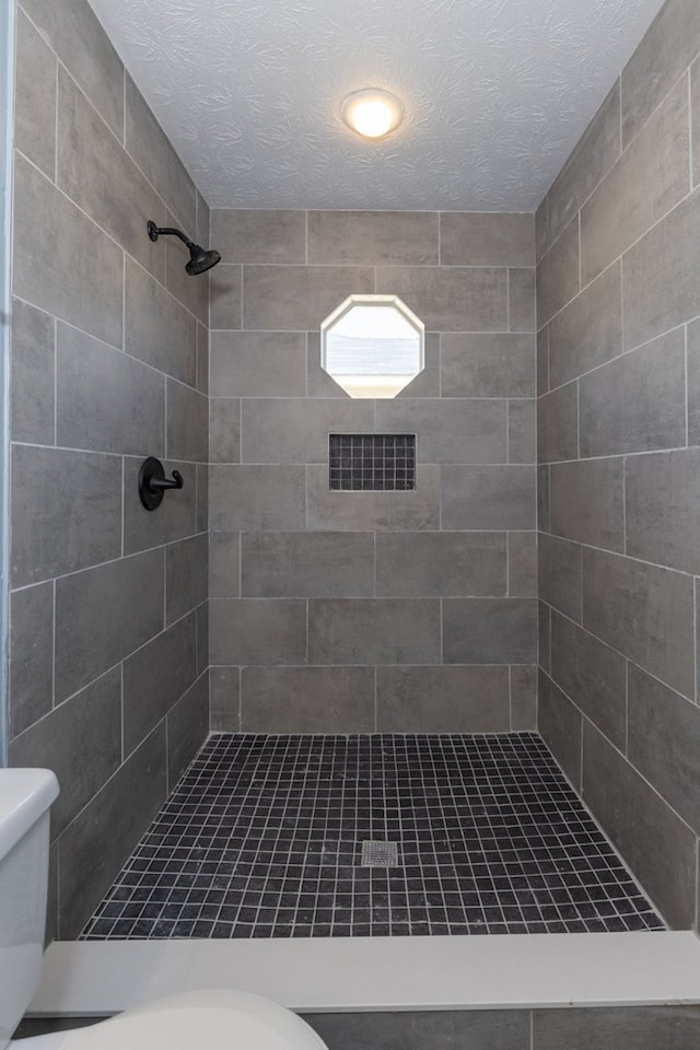 full bath with toilet, a tile shower, and a textured ceiling