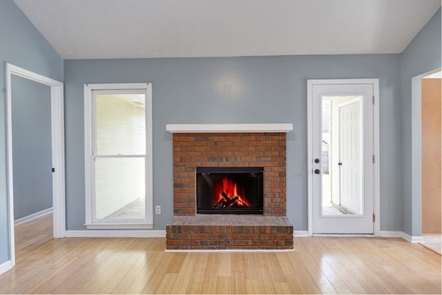 unfurnished living room with a brick fireplace, wood finished floors, baseboards, and a wealth of natural light