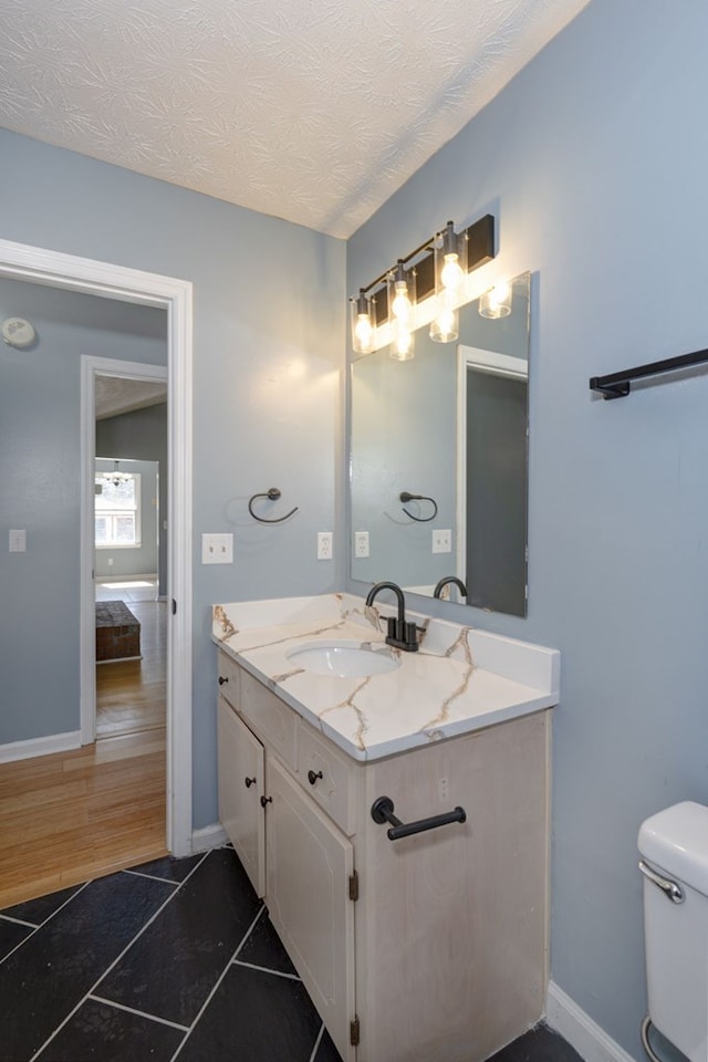 half bath with vanity, baseboards, tile patterned flooring, a textured ceiling, and toilet