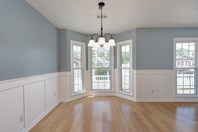 unfurnished dining area with visible vents, light wood-type flooring, wainscoting, an inviting chandelier, and a textured ceiling