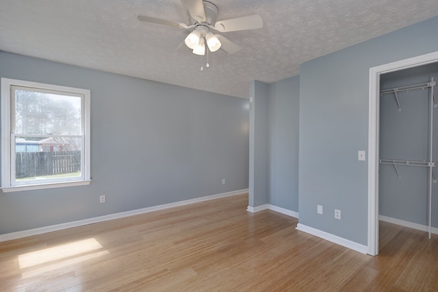 unfurnished bedroom featuring baseboards, a closet, a textured ceiling, a walk in closet, and light wood-type flooring