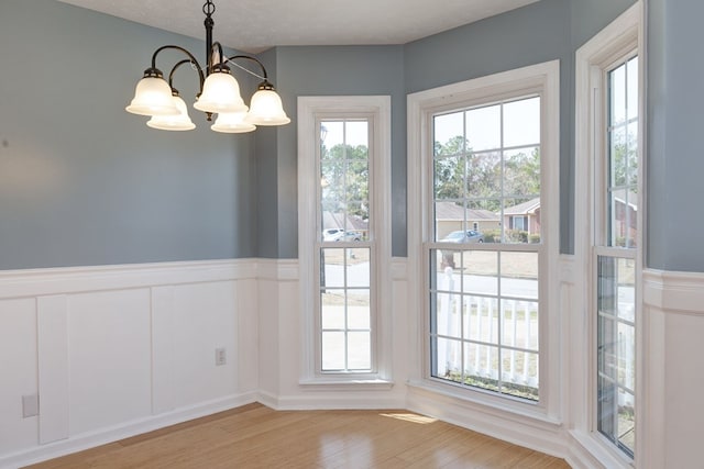 unfurnished dining area featuring a textured ceiling, wainscoting, light wood-type flooring, and a chandelier