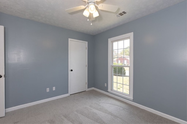 carpeted spare room featuring baseboards, visible vents, a wealth of natural light, and a textured ceiling