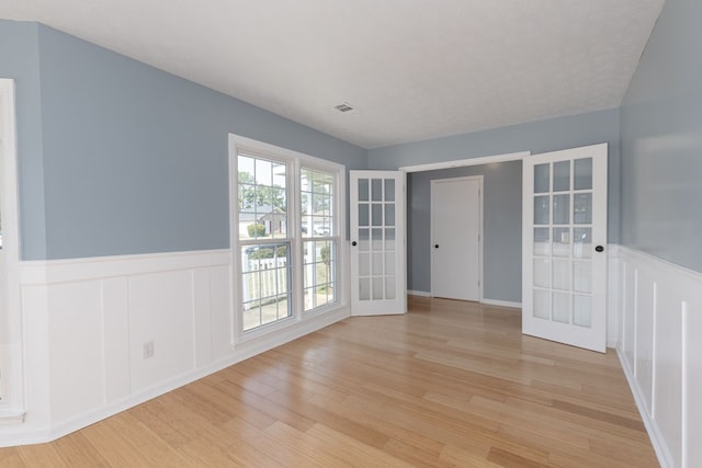 spare room with light wood-style flooring, french doors, visible vents, and wainscoting