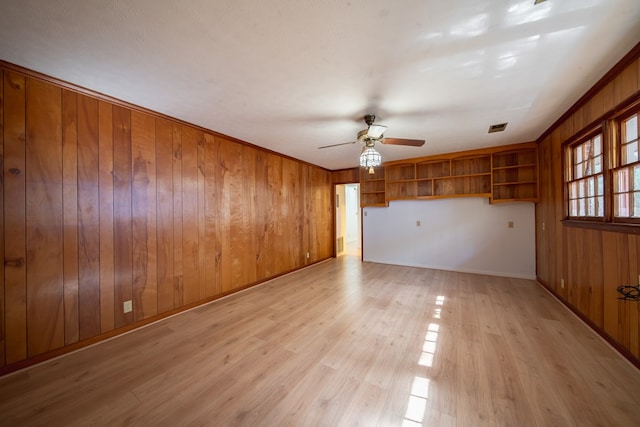 unfurnished room featuring crown molding, ceiling fan, wooden walls, and light hardwood / wood-style flooring